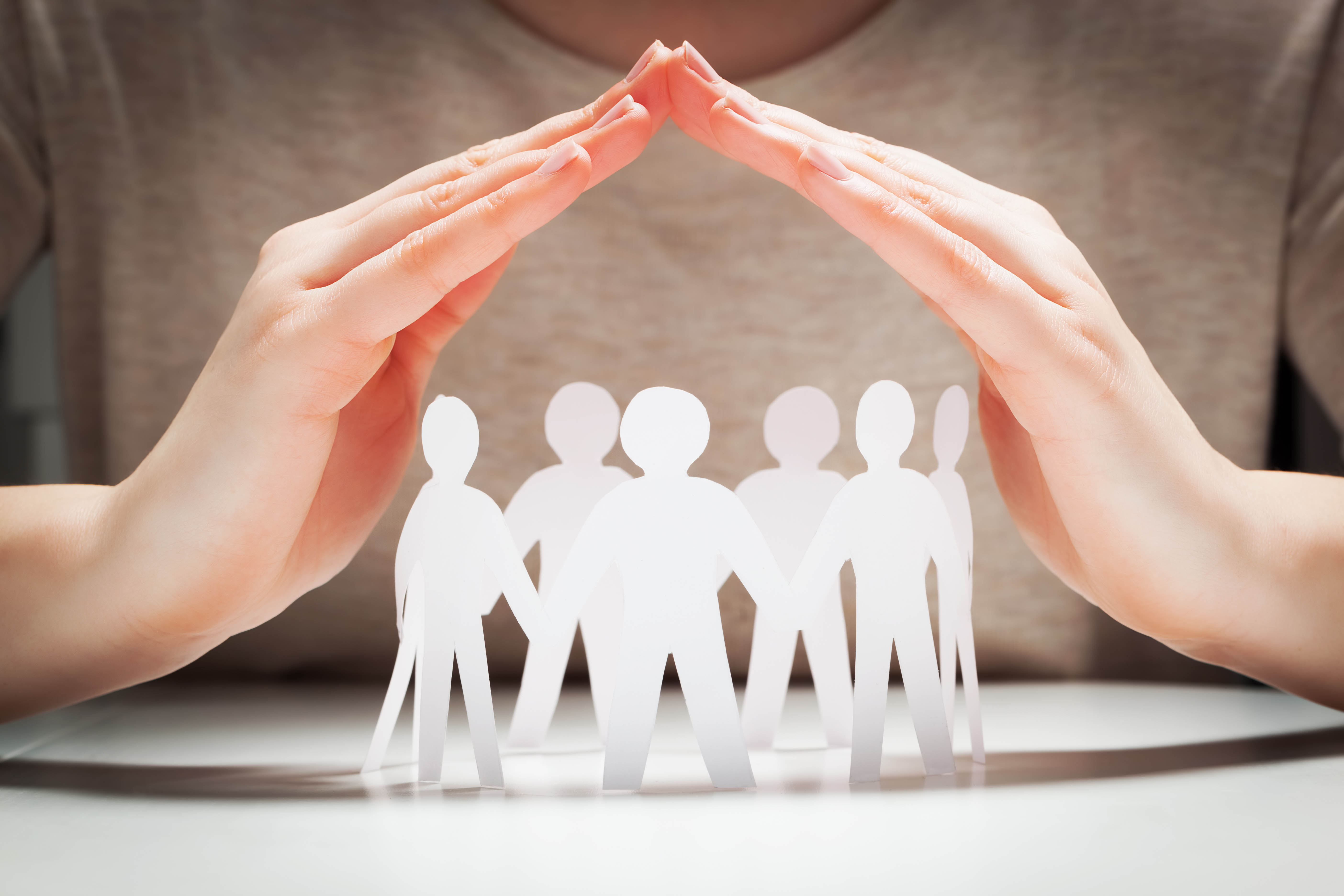 Person holding their hands, clasped, over top of a family of paper people
